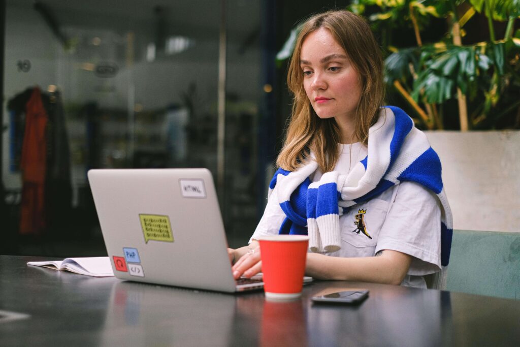 Person working on a laptop at a café table with a notebook and coffee, representing a small business owner or creative planning their website.